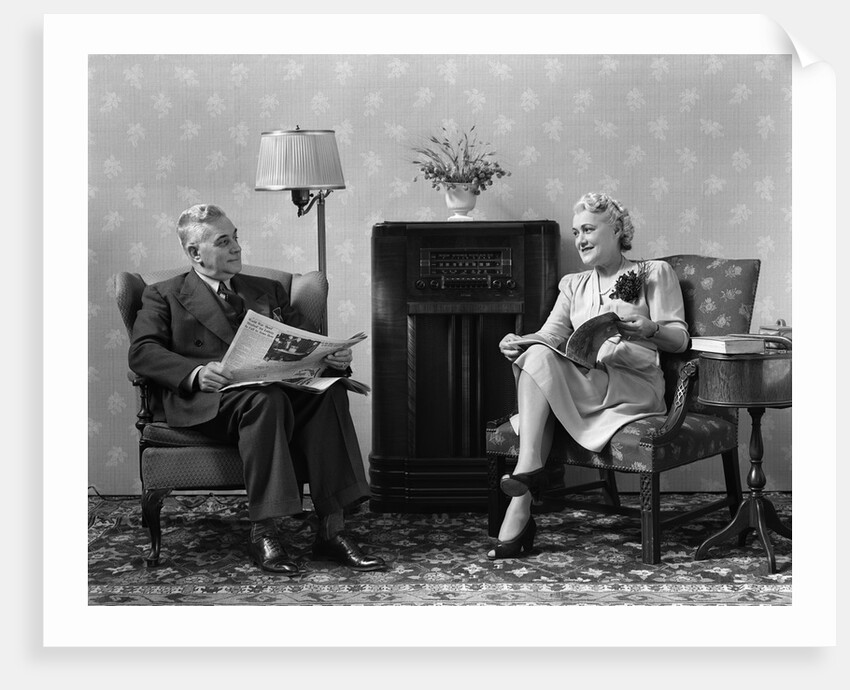 1940s Senior Couple Sitting In Living Room Reading Newspaper And Magazine Listening To Radio by Anonymous