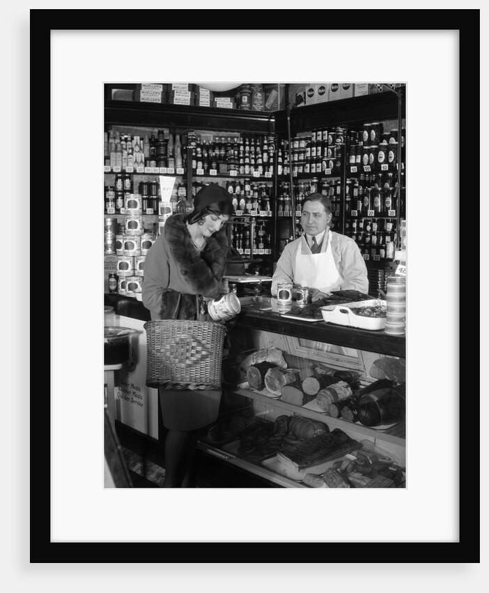 1920s Store Clerk Watching Woman Grocery Shopping Reading Label On Canned Goods by Anonymous