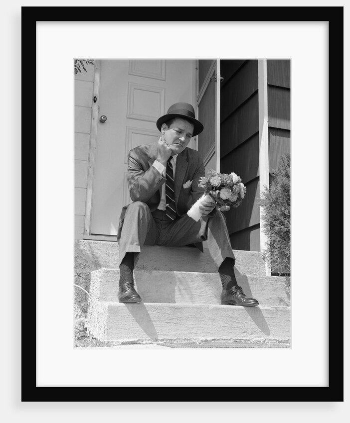 1950s Man In Suit And Hat Holding Flowers Sitting Outside Front Door On Steps Looking Sad by Anonymous