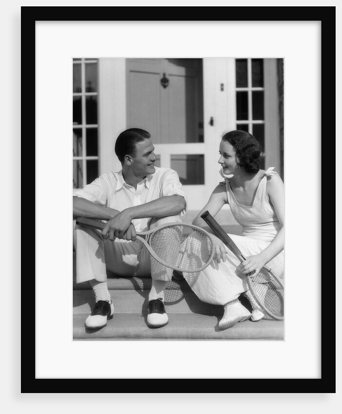 1930s Couple Man Woman In Tennis Whites Holding Racquets Sitting Talking On Steps In Front Of House Outdoor by Anonymous