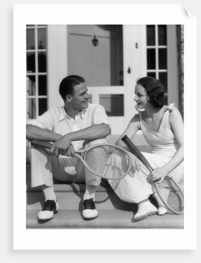1930s Couple Man Woman In Tennis Whites Holding Racquets Sitting Talking On Steps In Front Of House Outdoor by Anonymous
