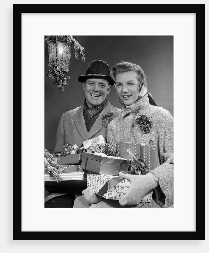 1950s Husband And Wife Carrying Armload Of Christmas Packages Standing In Snow Under Porch Light by Anonymous