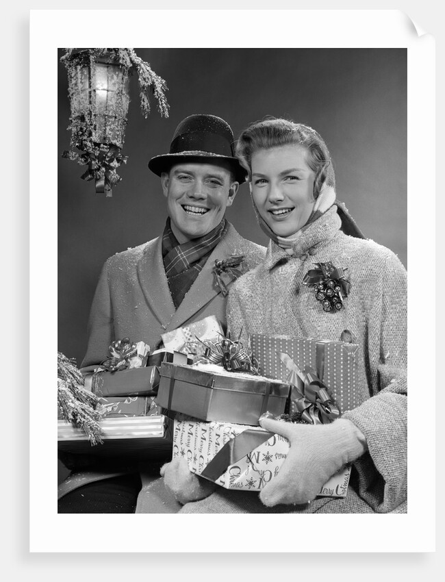 1950s Husband And Wife Carrying Armload Of Christmas Packages Standing In Snow Under Porch Light by Anonymous