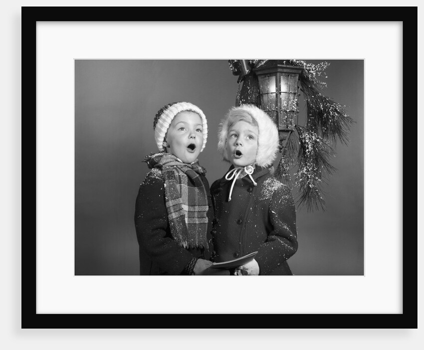 1960s Boy And Girl Singing Christmas Carol Together Under Snowy Outdoor Porch Light by Anonymous