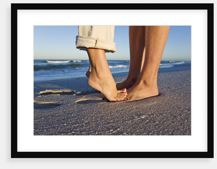 Feet of couple hugging on beach by Anonymous