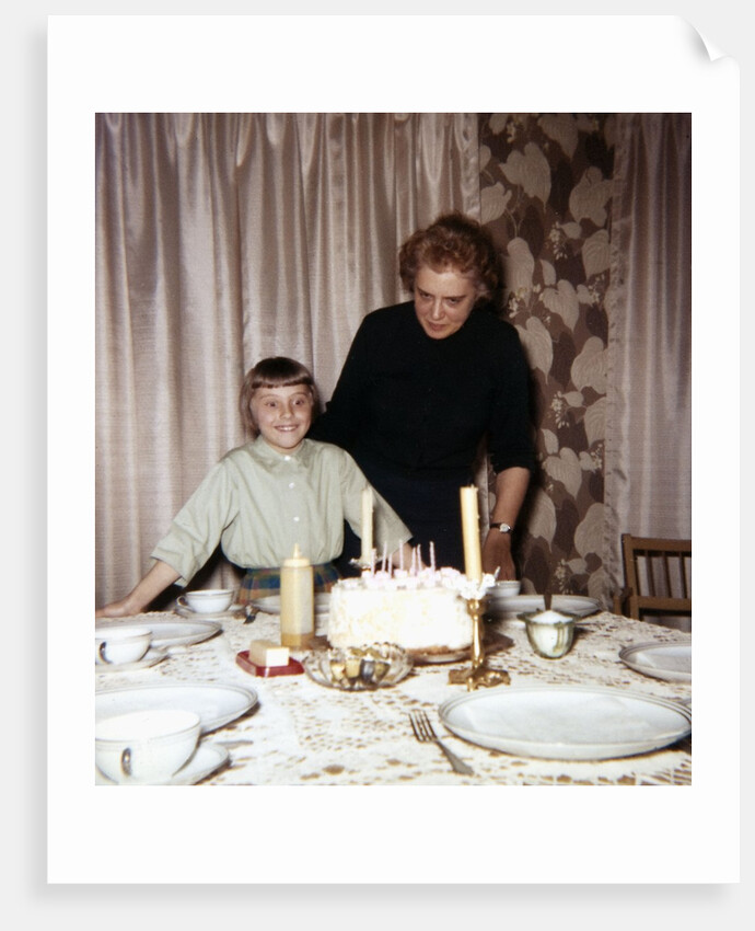 Nine year old girl is about to blow out the candles on her while her mom watches, ca. 1962 by Anonymous