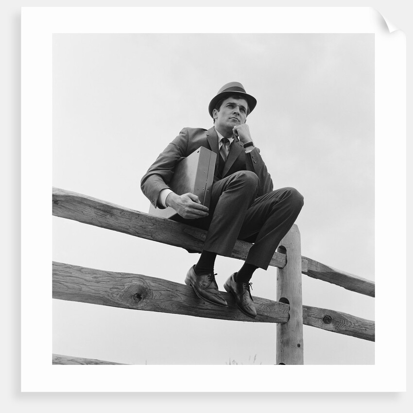 Businessman sitting on fence worried expression holding briefcase by Anonymous