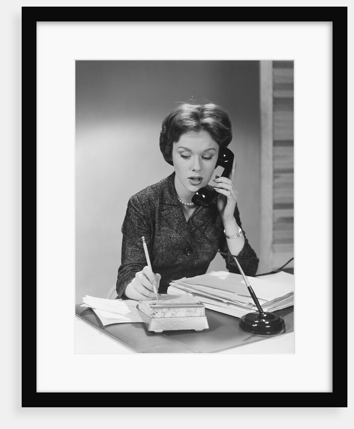 Brunette business woman sitting desk talking telephone writing note on calendar by Anonymous