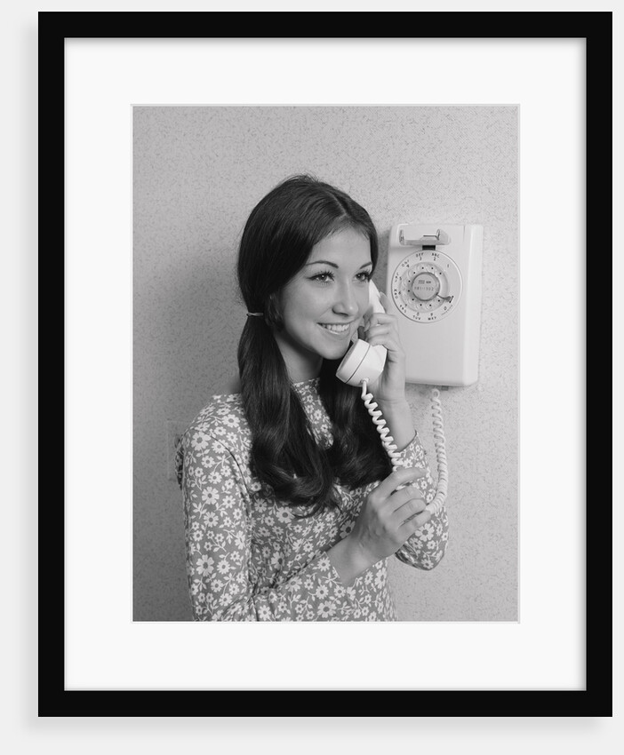 Smiling teenage girl talking on rotary wall telephone by Anonymous
