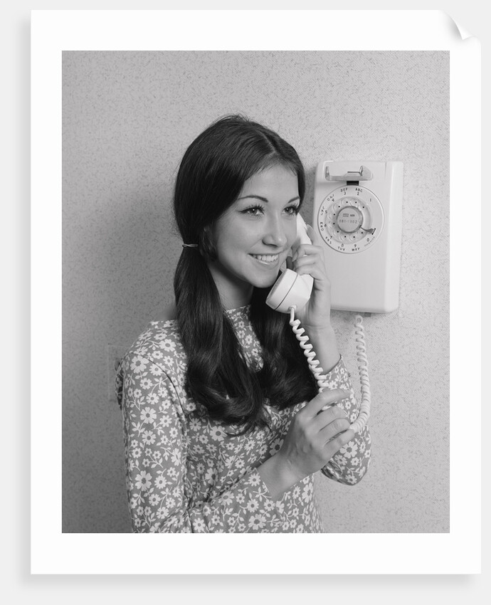 Smiling teenage girl talking on rotary wall telephone by Anonymous