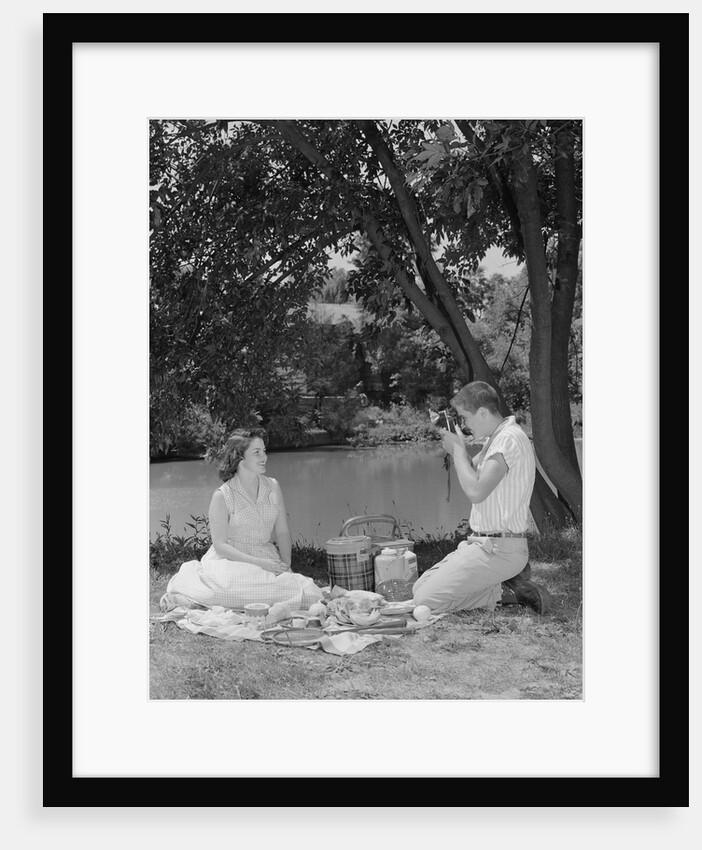 Teenage couple picnic boy taking photograph of girl outdoors by Anonymous