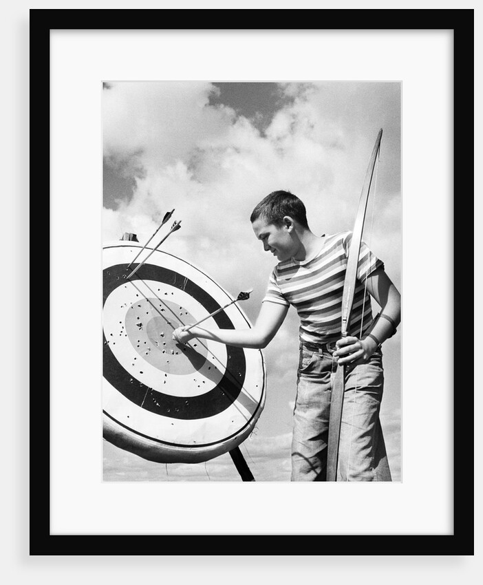 Boy jeans striped t-shirt holding bow & pulling arrow out of target bull's-eye by Anonymous