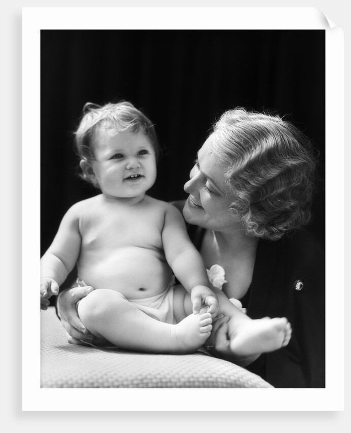 Blond woman mother smiling looking at baby sitting on pillow by Anonymous