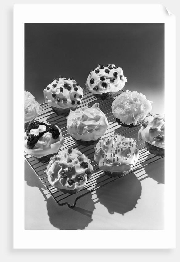Cupcakes on metal bakers cooling rack decorated with icing sprinkles chips by Anonymous