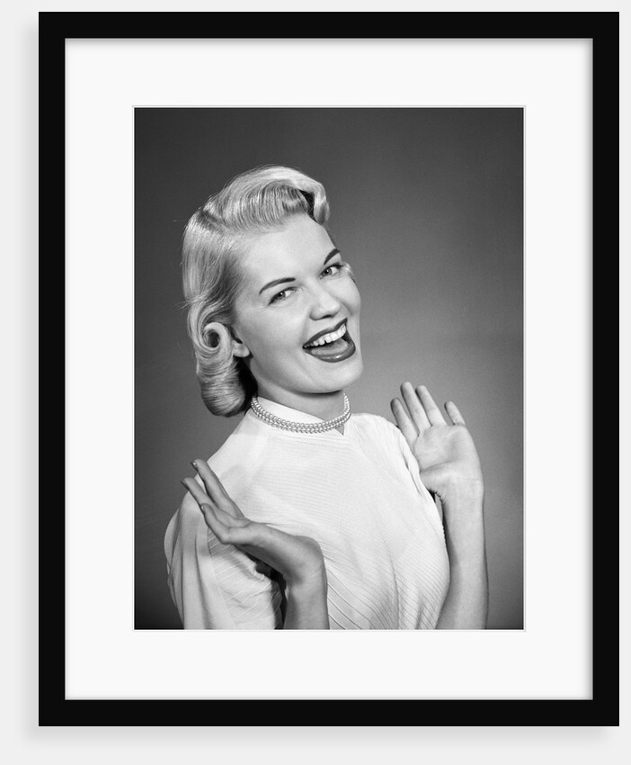 Woman wearing pearls smiling with hands up thumbs tucked under arm by Anonymous