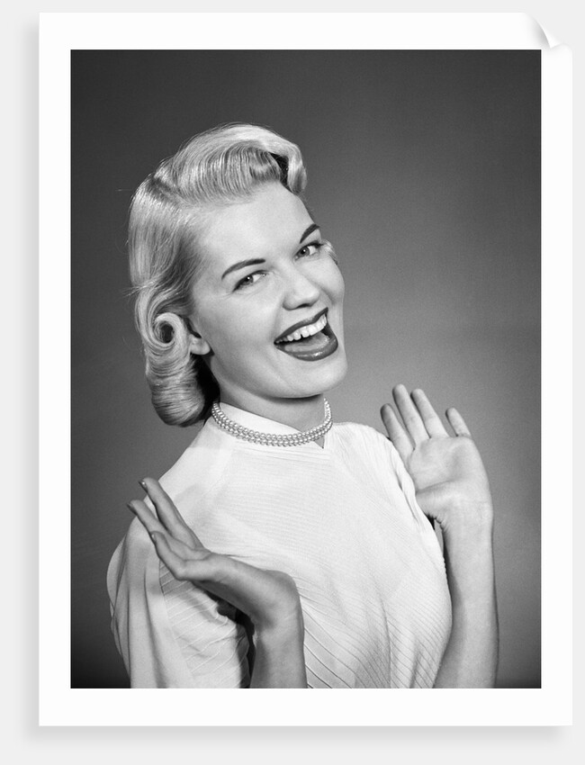 Woman wearing pearls smiling with hands up thumbs tucked under arm by Anonymous