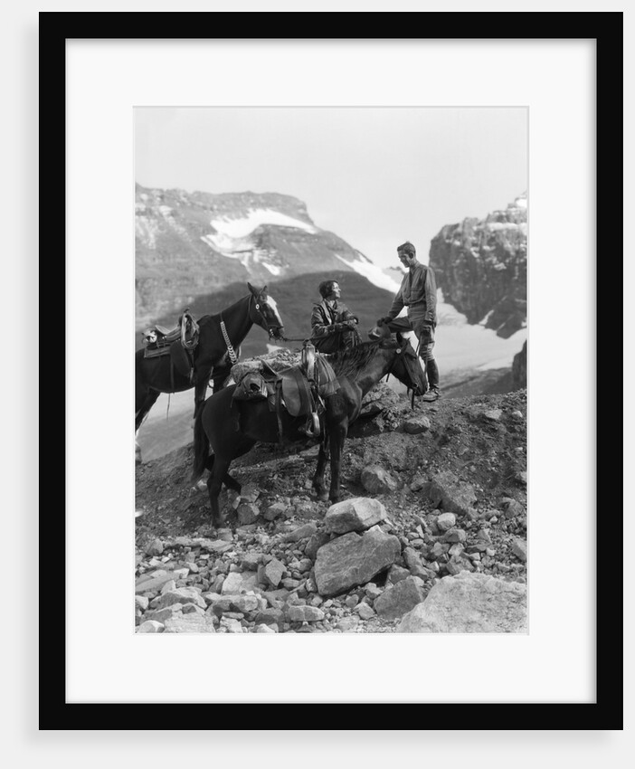 Couple man woman wearing riding gear jodhpurs boots spurs sitting standing on large rock by two horses by Anonymous