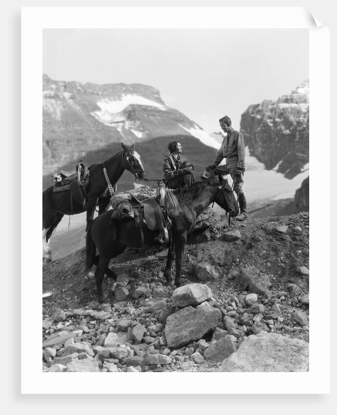 Couple man woman wearing riding gear jodhpurs boots spurs sitting standing on large rock by two horses by Anonymous