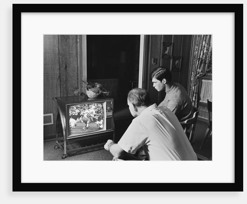 Teen boy watching football game on television with adult dad by Anonymous
