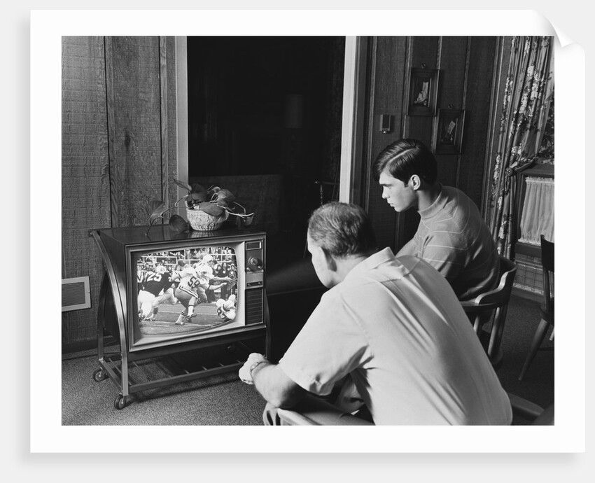 Teen boy watching football game on television with adult dad by Anonymous