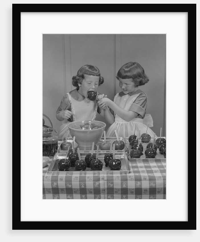 Two twin girls eating making candy apples in kitchen by Anonymous