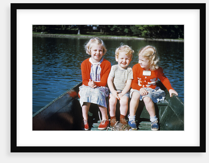 Boy and two girls in red sweaters sitting in back of rowboat by Anonymous