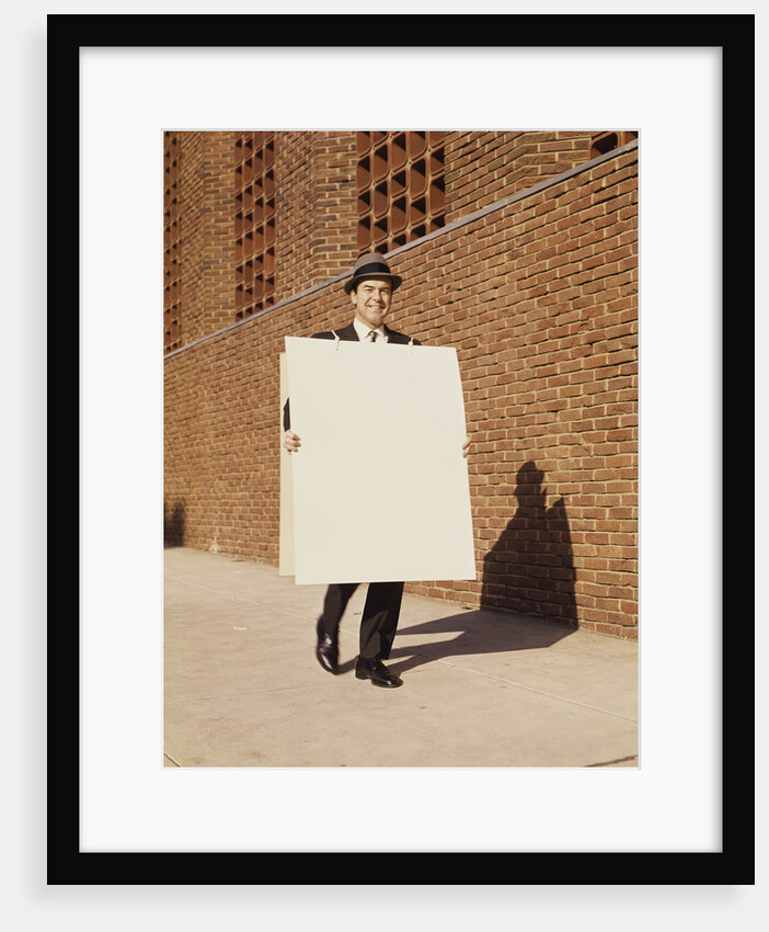 Smiling man wearing suit necktie and hat walking carrying large sandwich board by Anonymous