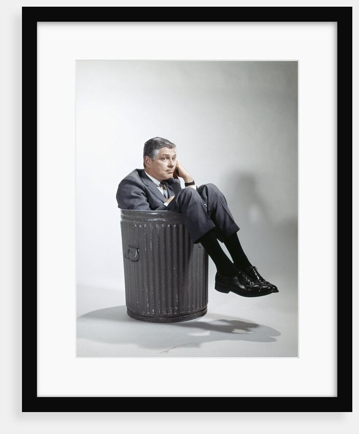 Sad man in business suit sitting in trash garbage can by Anonymous