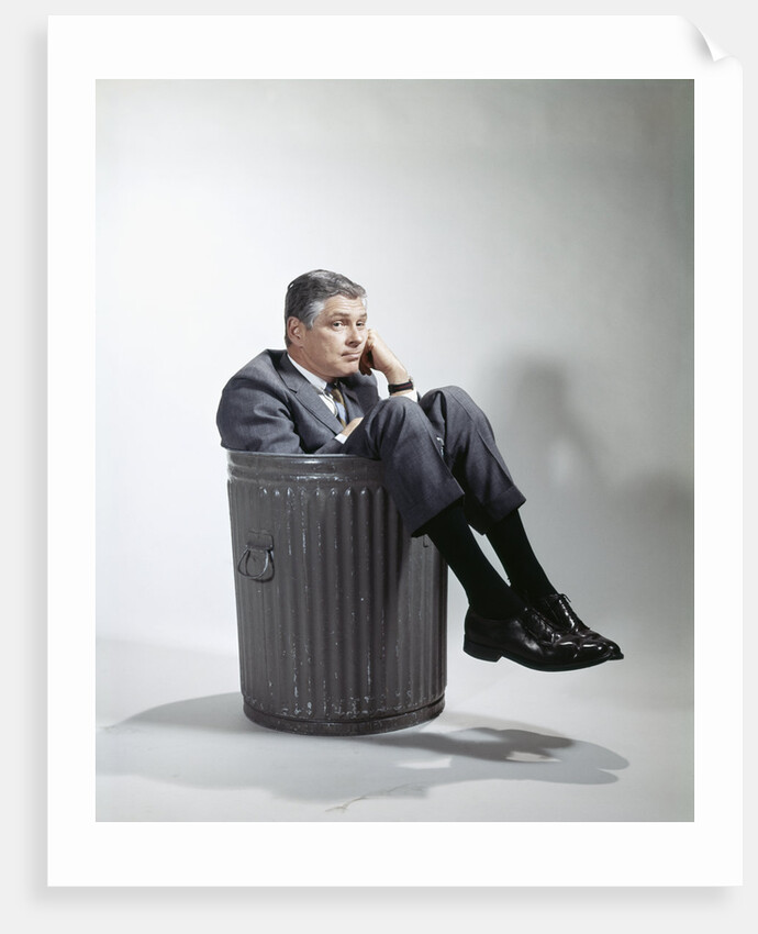 Sad man in business suit sitting in trash garbage can by Anonymous