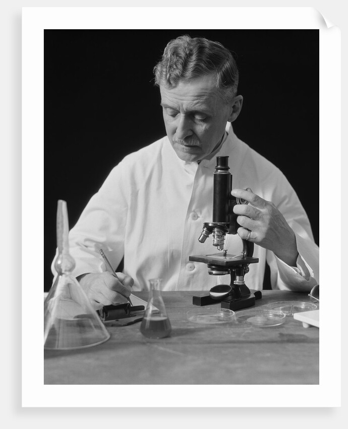 Male scientist wearing white lab coat writing data on clip board holding focus control of microscope by Anonymous