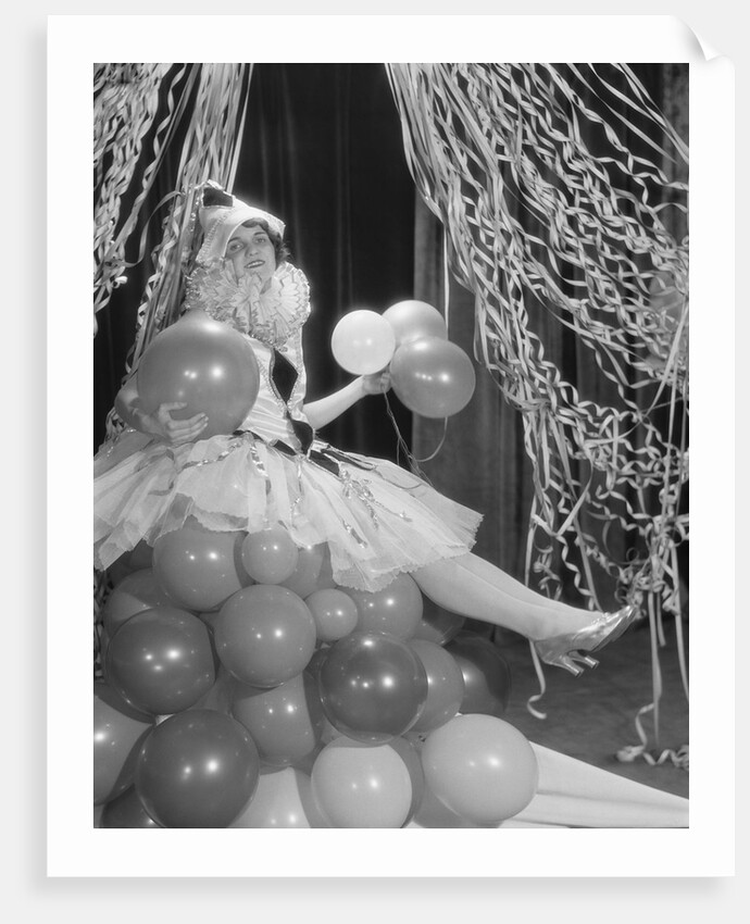 Woman dressed in harlequin costume sitting on stack of balloons by Anonymous