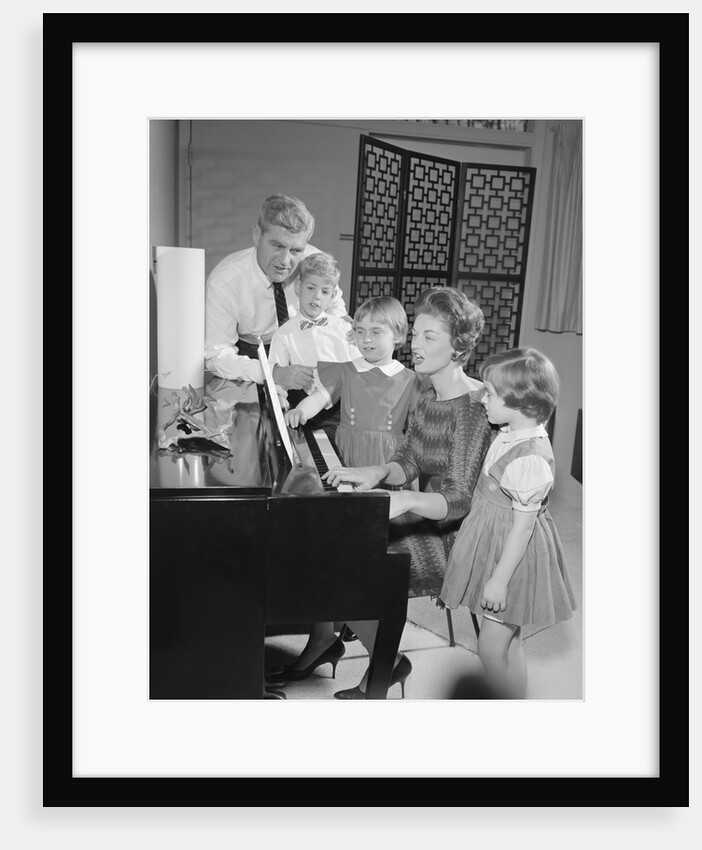 Family standing around piano singing by Anonymous