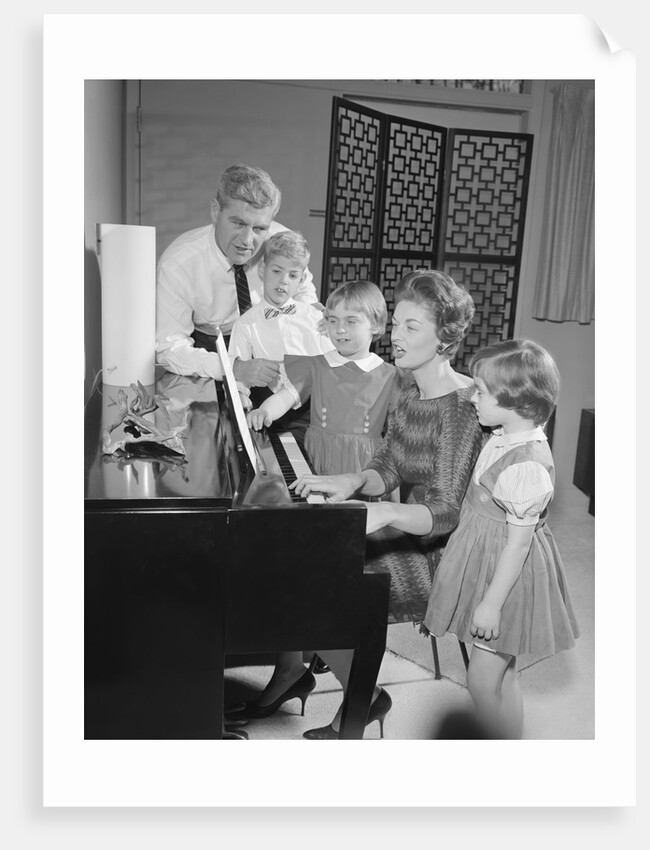 Family standing around piano singing by Anonymous