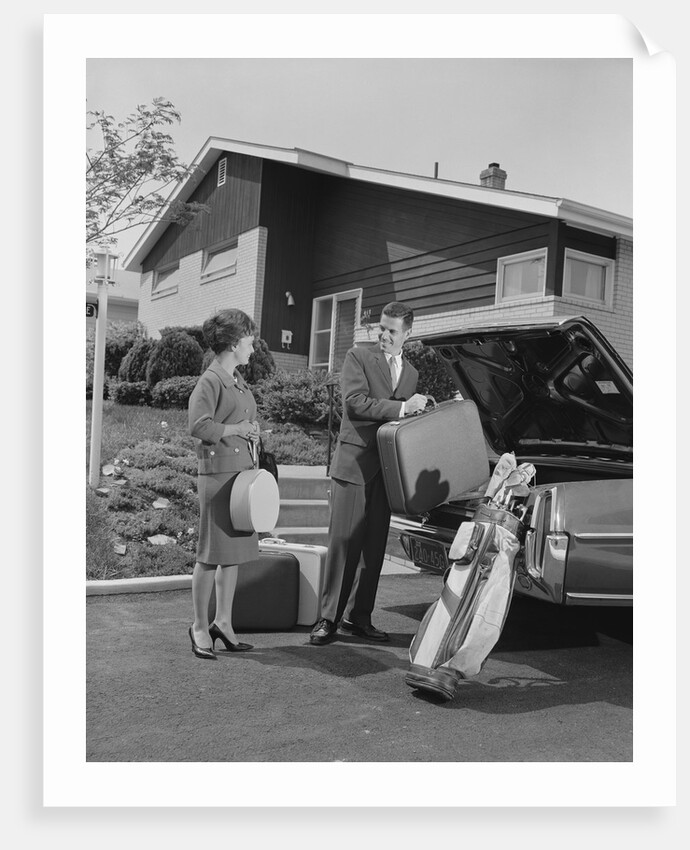 Couple man woman packing luggage into car trunk by suburban house by Anonymous