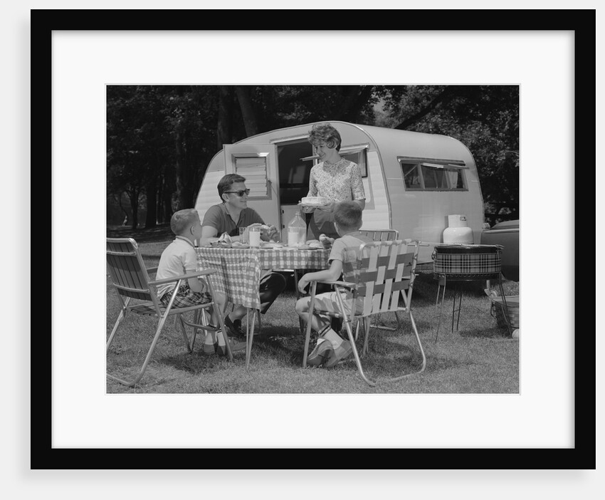 Family camping eating meal beside rv camper by Anonymous