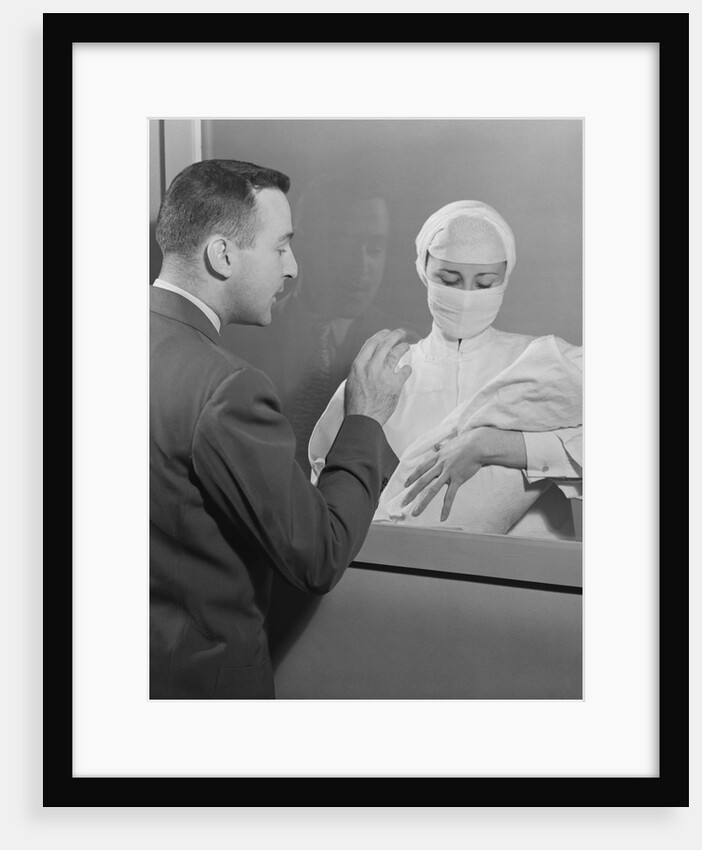 Female nurse holding infant up to father at nursery window by Anonymous