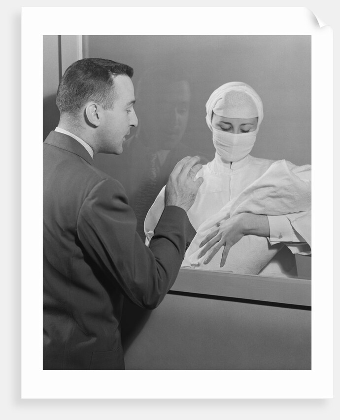 Female nurse holding infant up to father at nursery window by Anonymous