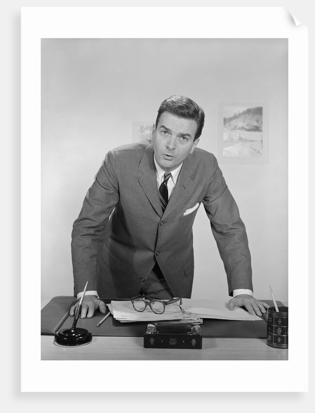 Businessman leaning over desk serious expression looking forward by Anonymous