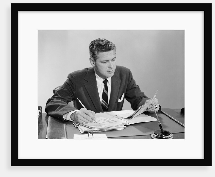 Businessman at desk looking over files papers making notes with pencil by Anonymous
