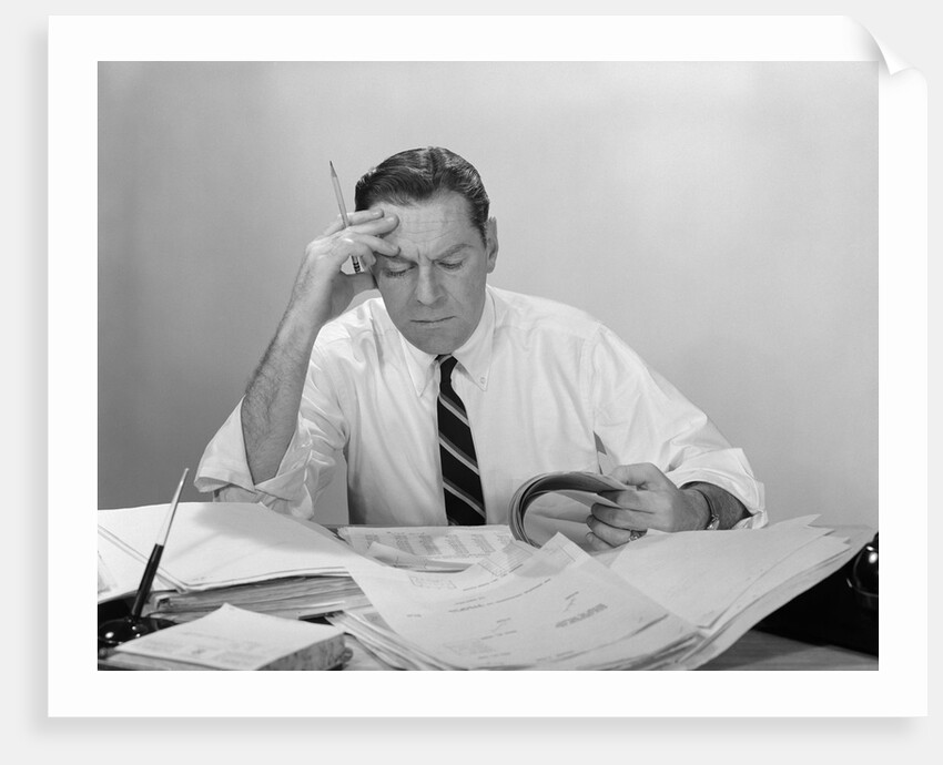 Businessman desk full papers hand to forehead serious expression by Anonymous