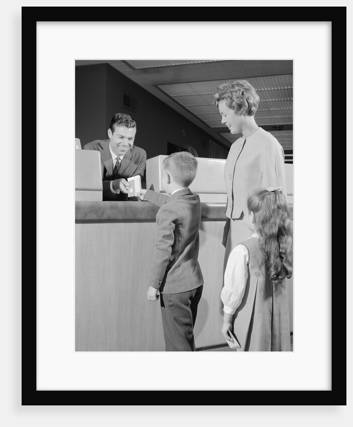 Mother two children boy handing banking deposit to male bank teller by Anonymous
