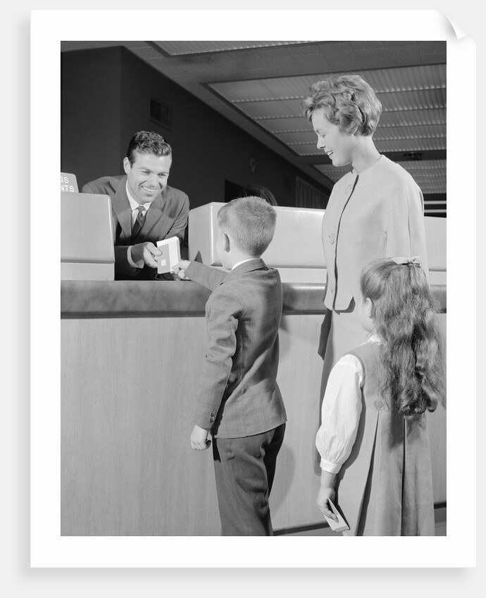 Mother two children boy handing banking deposit to male bank teller by Anonymous