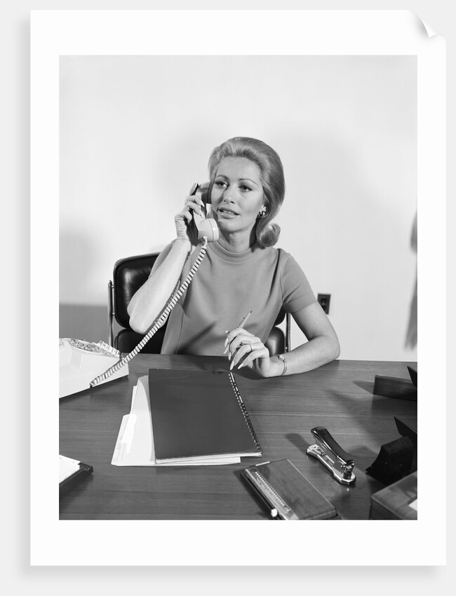 Blond businesswoman talking on telephone sitting at desk by Anonymous