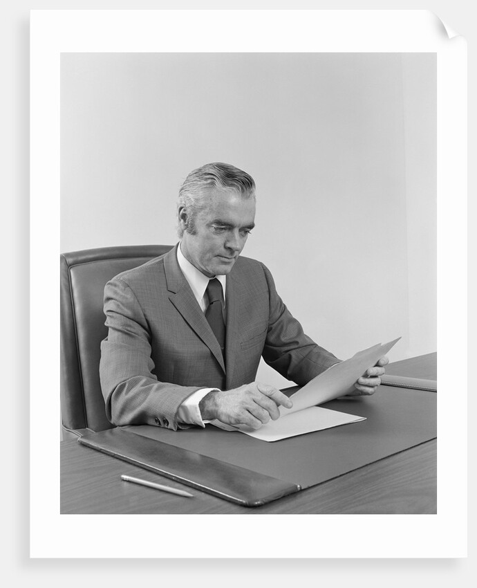 Businessman executive middle aged sitting at desk reading papers by Anonymous