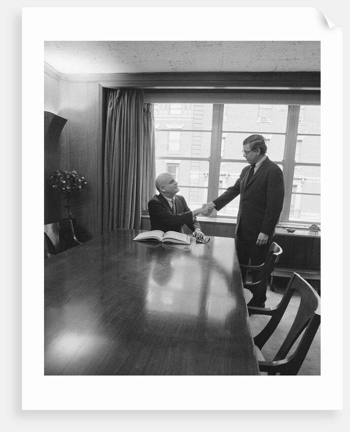 Two men one seated shaking hands long wooden conference table by Anonymous