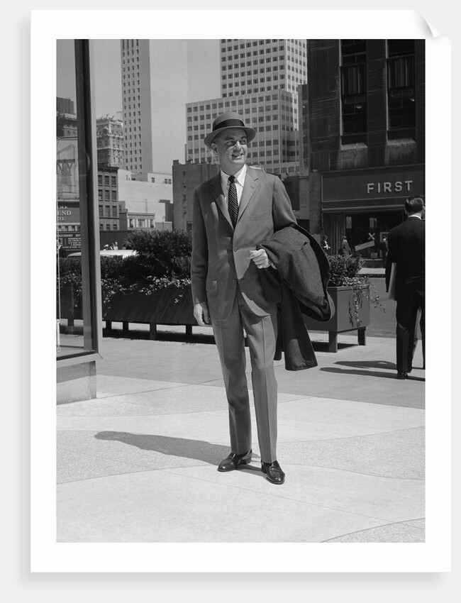 Businessman wearing suit hat carrying top coat standing on city street by Anonymous