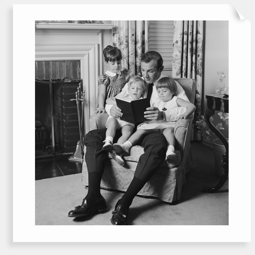 Man father sitting in chair with three children reading book by Anonymous