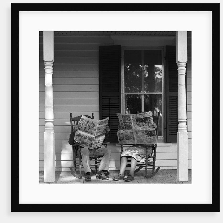 Couple man woman sitting on porch in rocking chairs holding newspapers up hiding their faces by Anonymous