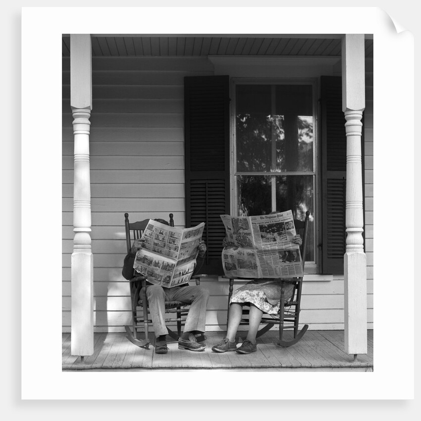 Couple man woman sitting on porch in rocking chairs holding newspapers up hiding their faces by Anonymous