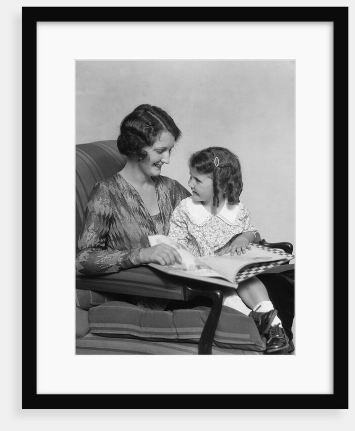 Mother & daughter smiling sitting in chair reading book by Anonymous